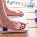 Female feet standing on mechanical scales, dumbbells and measuring tape. Concept of slimming and weight loss